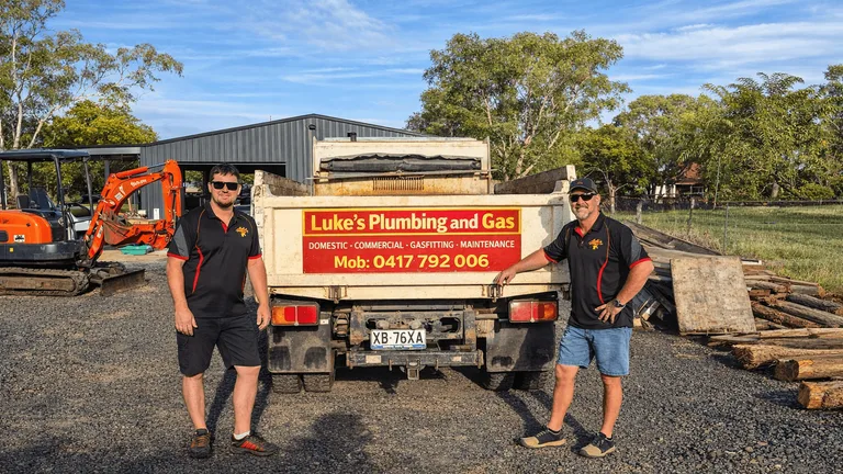 Luke's Plumbing and Gas signed tipper truck and Kubota excavator in a sunlit Toowoomba yard