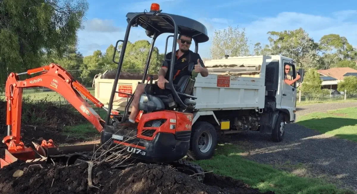 Luke with a thumbs up beside his 1.7-tonne excavator on a job site